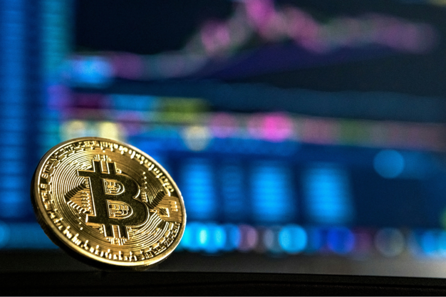 Bitcoin dorato in primo piano con grafici finanziari sfocati sullo sfondo, rappresentazione del trading e delle criptovalute