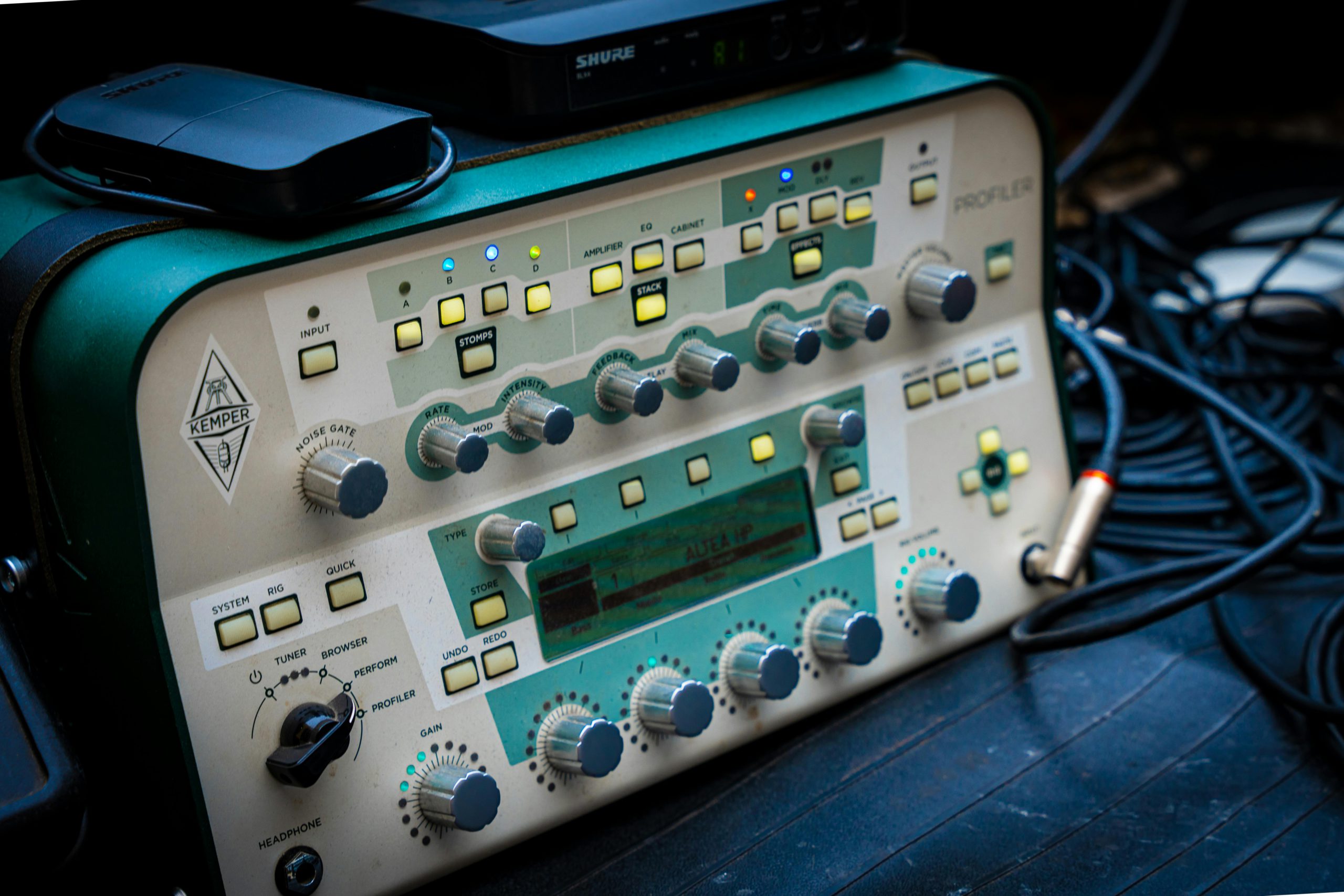 Kemper Profiler, processore di effetti e modellatore di amplificatori per chitarra, con manopole e pulsanti illuminati, circondato da cavi audio.