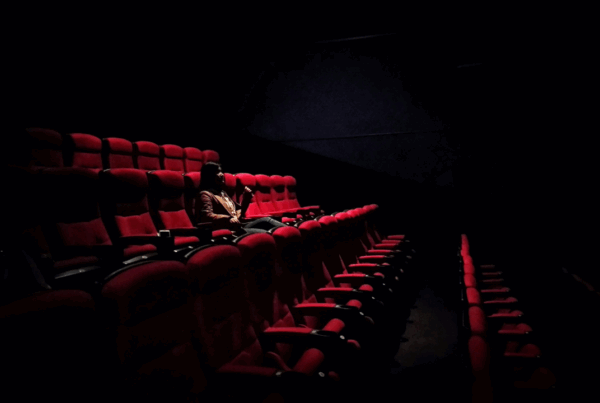 Woman sitting alone in an empty movie theatre with red seats, dark and reflective atmosphere while watching Nolan's The Odyssey .